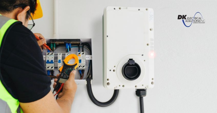 En elektriker utför installation och kontroll av en laddbox för elbilar på en arbetsplats.